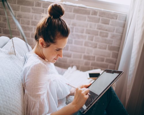 Student taking notes on a tablet during an online class at home
